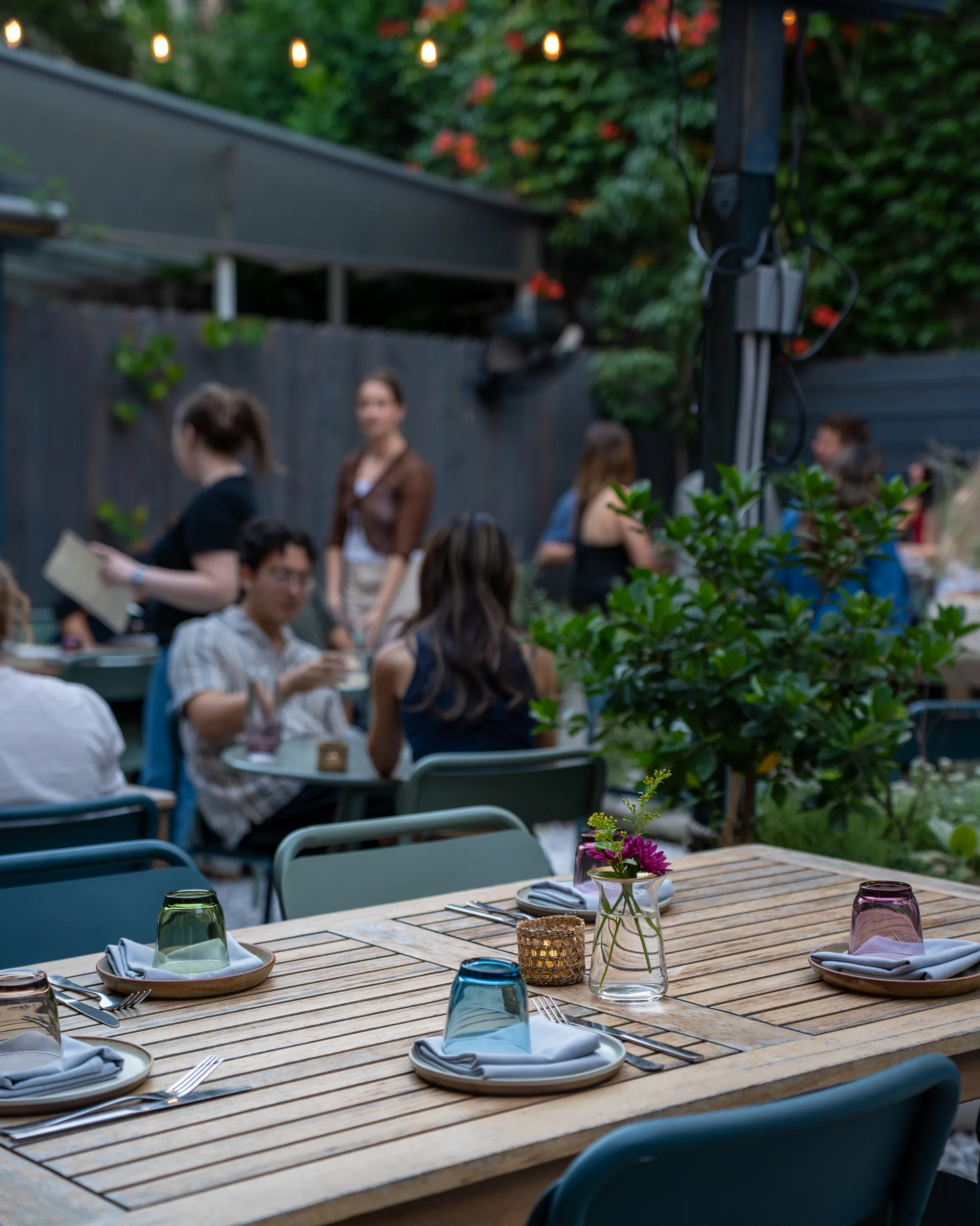 A table set for dinner in the Sawa garden, with guests under string lights behind it